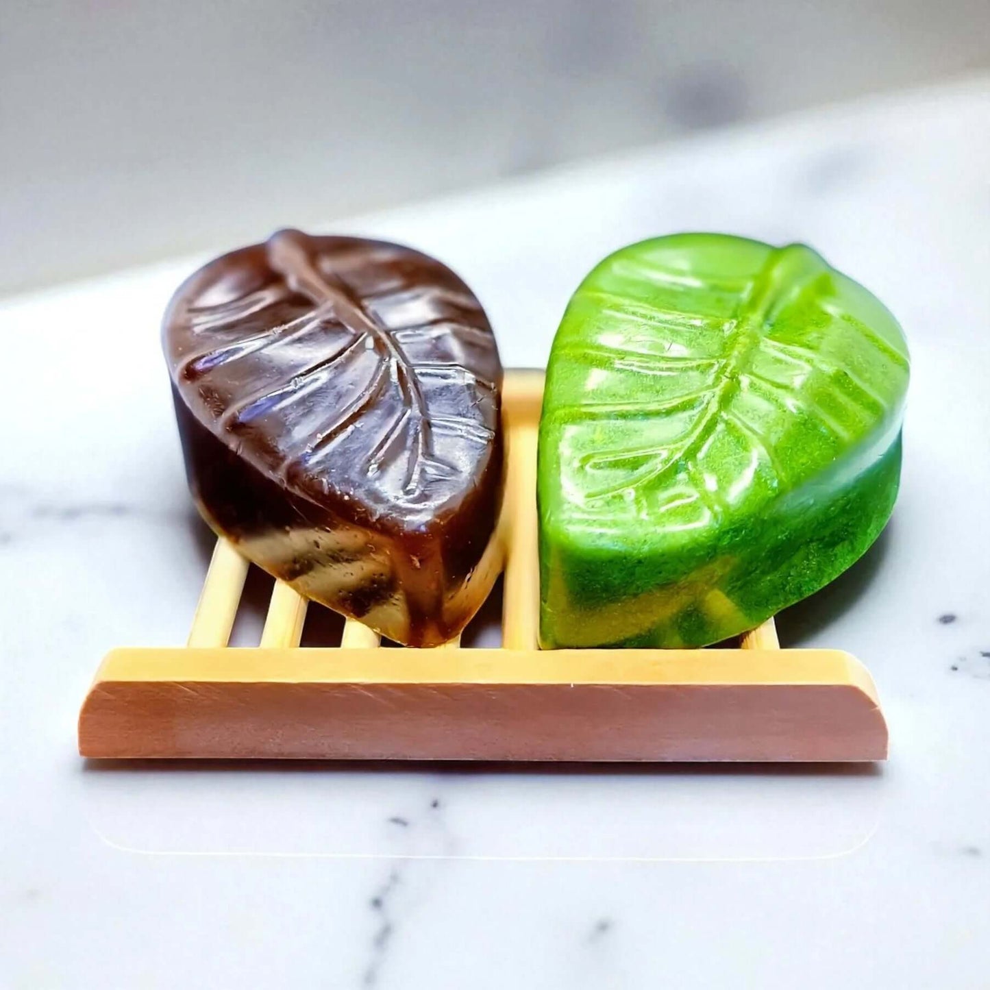 Aloe Vera and Neem soap bars shaped like leaves on a bamboo soap dish, showcasing vibrant green and brown colors.